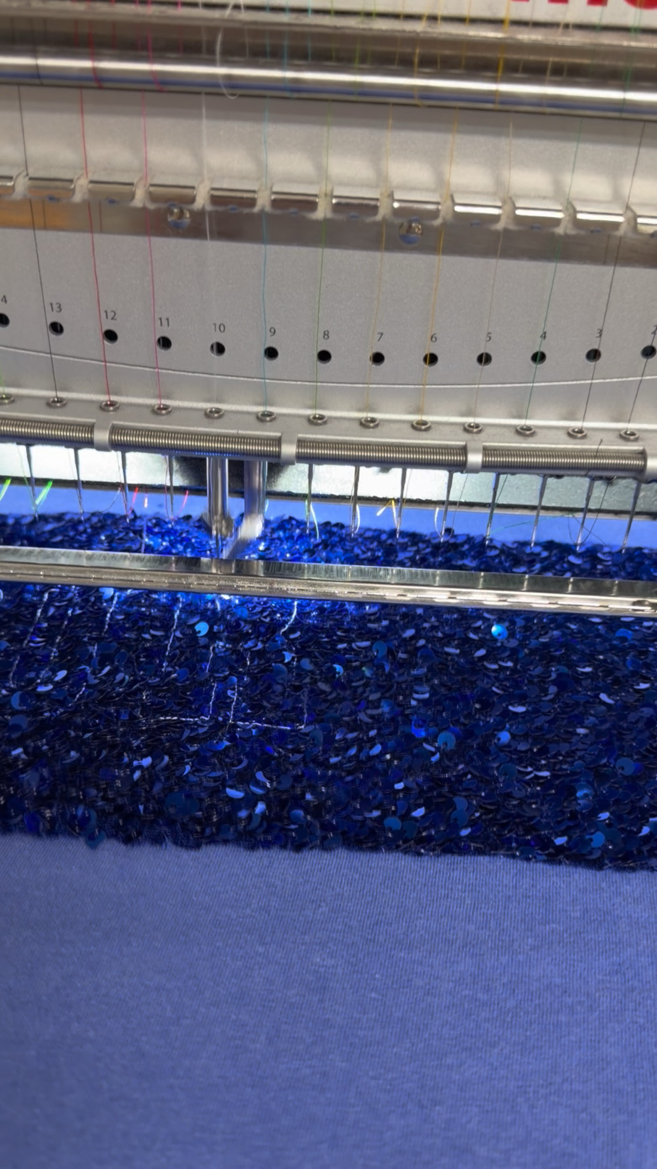Captain Hawk Designs embroidery machine stitching blue sequins onto a Registered Nurse crewneck t-shirt fabric.