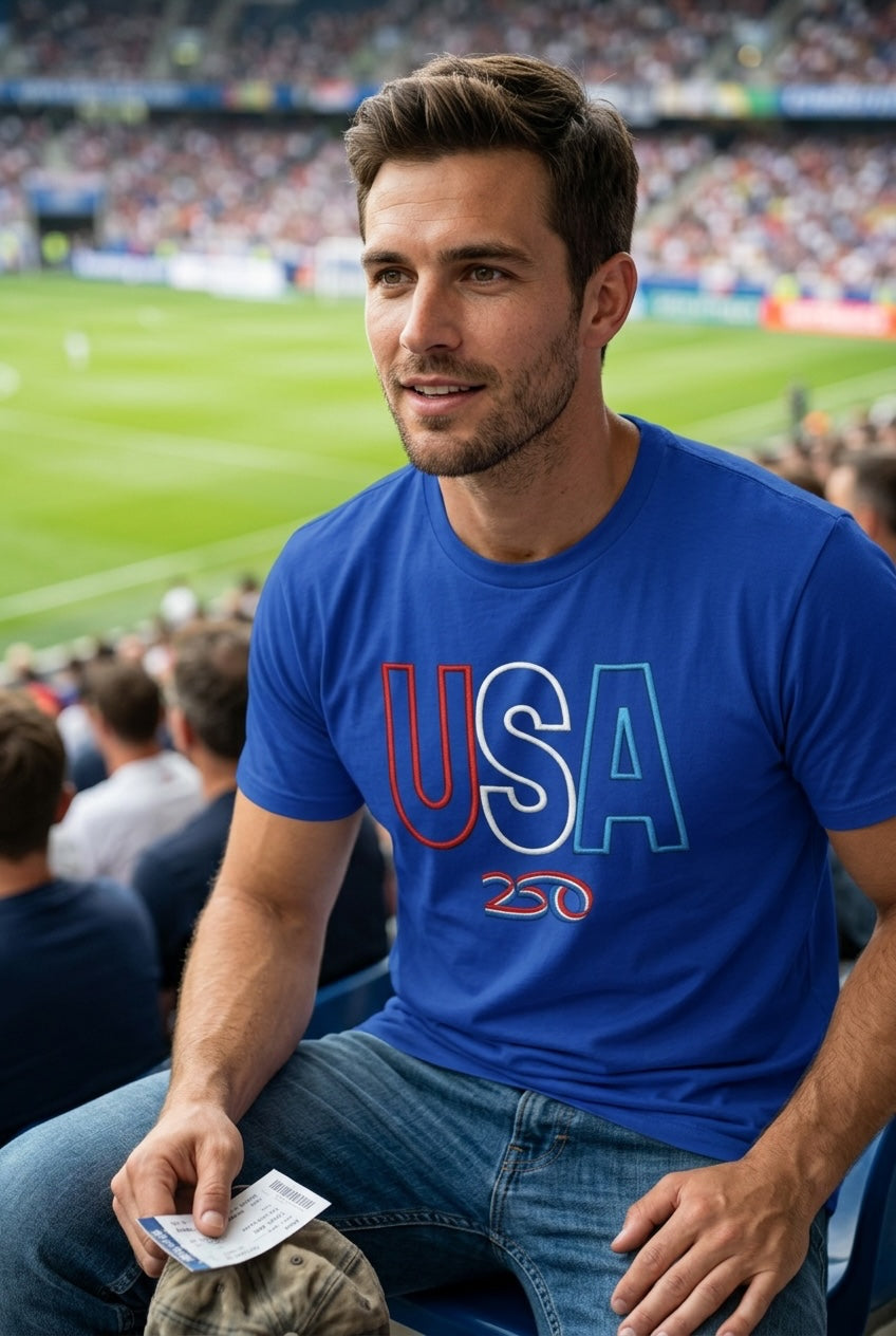 Captain Hawk Designs blue crewneck t-shirt with USA 250 embroidery worn by a man at a stadium